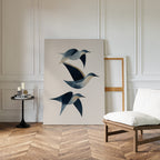 A minimalist room with white paneled walls, wood floors, a cushioned chair, and a small black side table with candles. The Abstract Birds in Motion Canvas Art leans stylishly against the wall, adding a modern touch.