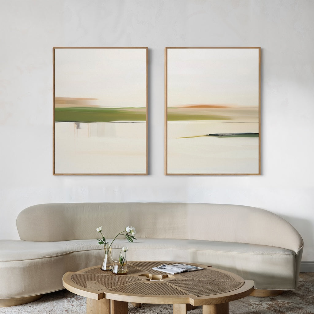 A modern living room features a curved beige sofa, a round wooden coffee table with two vases of flowers, and the Abstract Horizons Set of 2—minimalist abstract landscape paintings in wooden frames—hanging on a white wall.