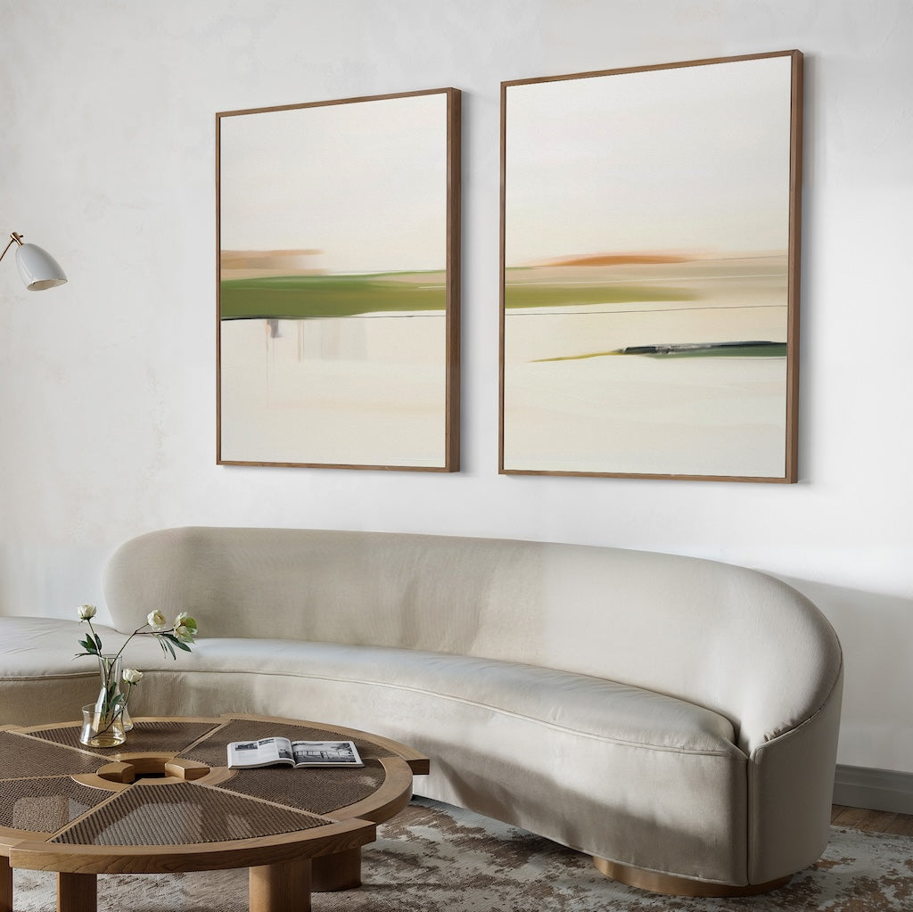 A minimalist living room with a curved beige sofa, a round wooden coffee table with a vase and books, and the Abstract Horizons Set of 2—modern canvas wall art in wooden frames featuring abstract landscapes on a white wall.