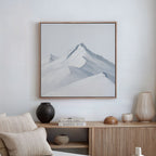 A minimalist living room features Alpine Ascent Abstract Canvas Art, neutral decor, a wooden sideboard, and vases by a stack of books including KINFOLK TRAVEL, creating a calm and modern atmosphere.