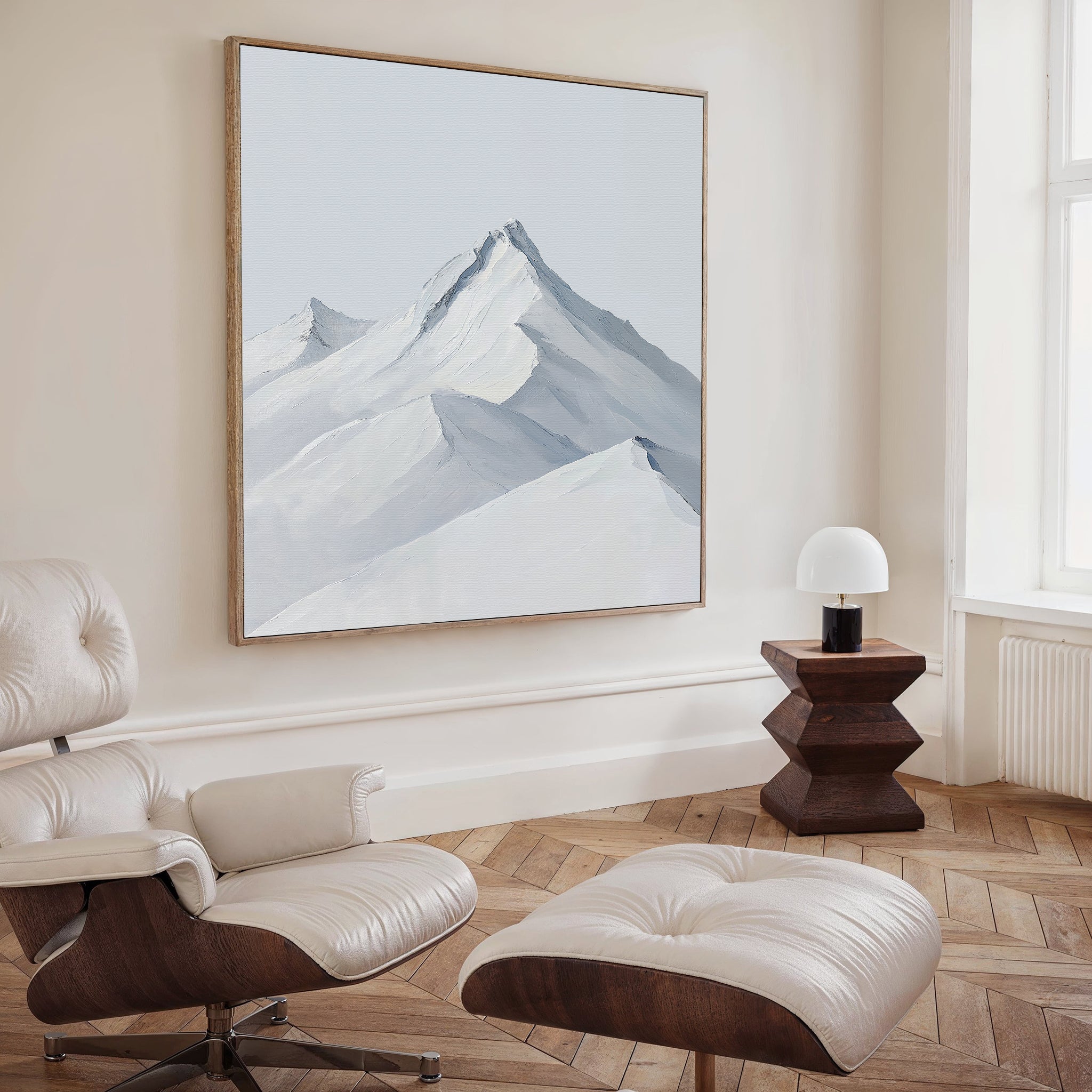 A modern living room with a white leather lounge chair and ottoman, wooden side table with a small white lamp, and the Alpine Ascent Abstract Canvas Art of snowy mountains completes the perfect decor.