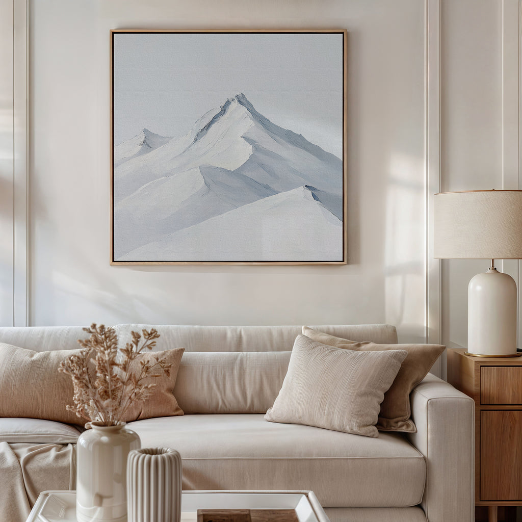 A modern living room with a white sofa, beige cushions, and a side table with a white lamp. The Alpine Ascent Abstract Canvas Art of snowy mountains elevates the decor, while dried flowers in a vase accent the coffee table.
