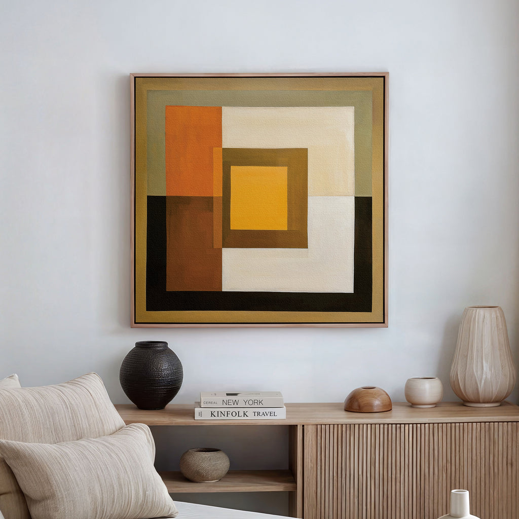 A modern living room showcases the Amber Layers Abstract Canvas Art—an earthy geometric painting—above a light wood sideboard adorned with neutral vases and stacked books, while a beige couch with textured pillows is partially visible.
