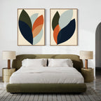 A modern bedroom with an olive-green bed, white bedding, and two beige nightstands with matching lamps. Above the bed, the Autumn Layers Set of 2 adds a touch of modern style with abstract green, orange, navy, and light blue art.