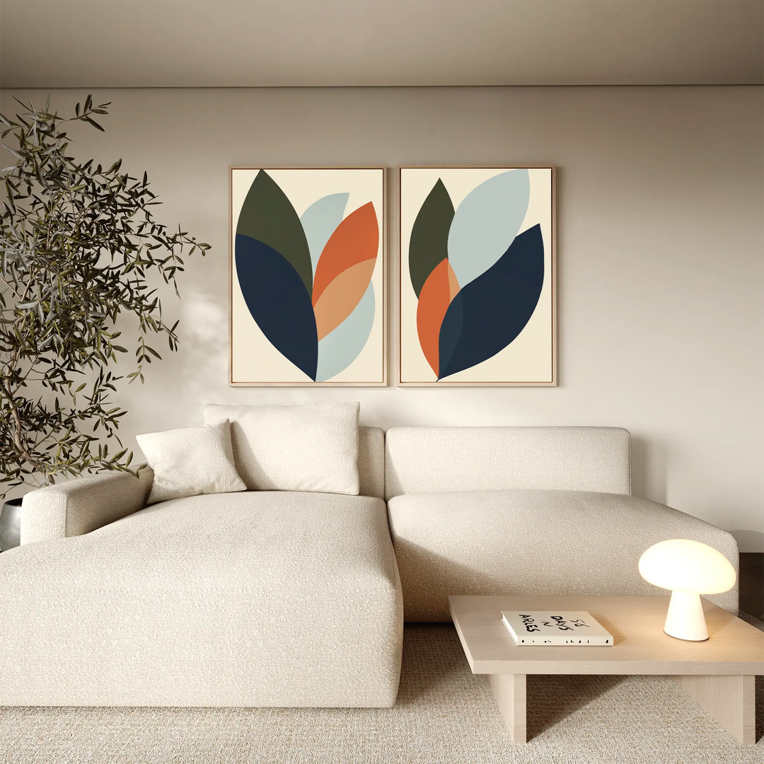 A modern living room featuring a cream sectional sofa, light wood coffee table with magazines and lamp, an indoor plant, and the Autumn Layers Set of 2—striking leaf-themed wall art that enhances the room’s decor.