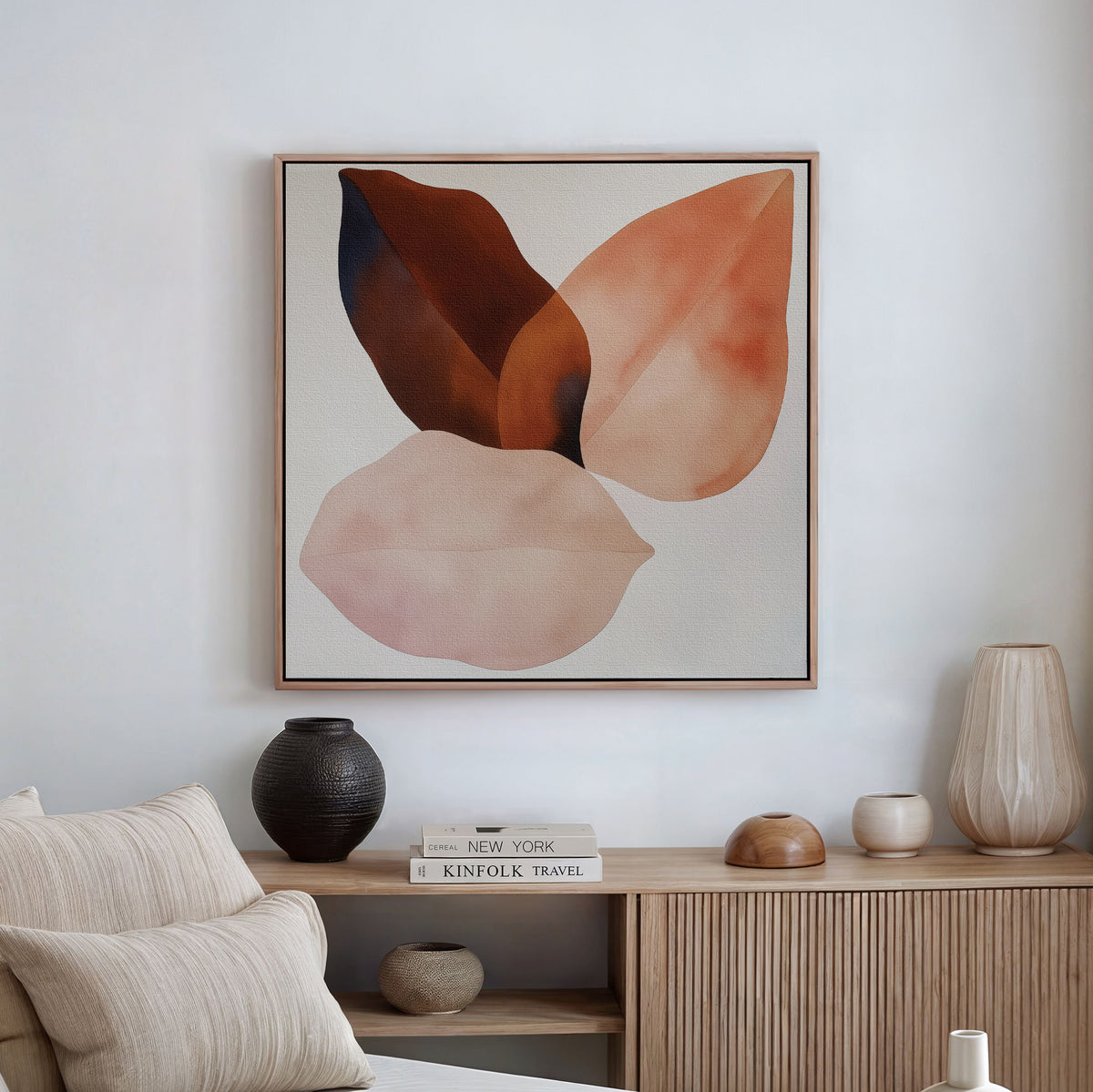 A minimalist living room showcases a beige couch, pale cushions, a light wood sideboard with neutral vases and books, and Autumn Petals Canvas Art in earthy tones on a white wall.