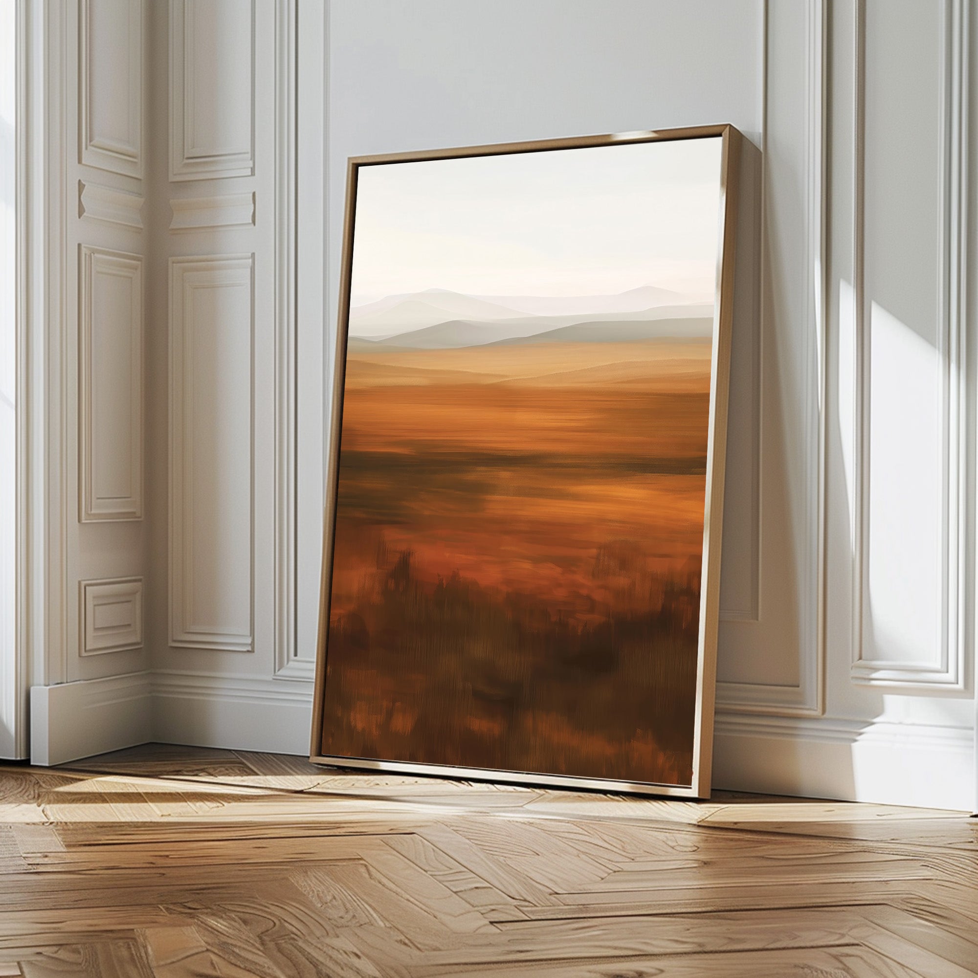 The Autumn Plains Abstract Canvas Art, with warm blurred tones of brown fields and distant hills, is framed and leans against a white wall on a wooden floor in a bright, elegant room.