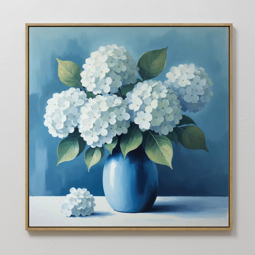 Azure Cluster Canvas Art showcases white hydrangea flowers with green leaves in a blue vase against a soft blue background. Framed in light wood, this floral wall art features a single bloom beside the vase, ideal for living room decor.