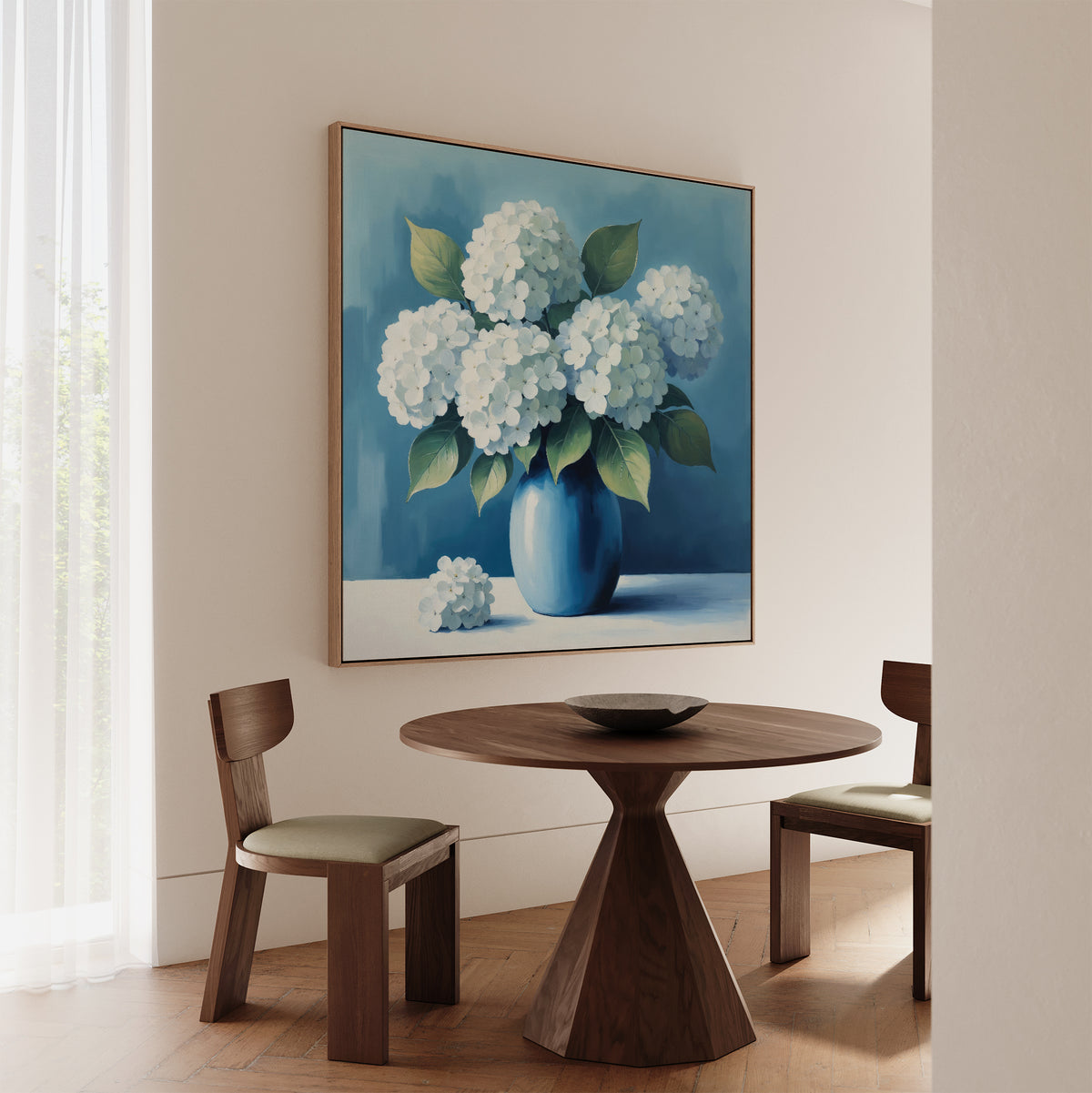 A cozy nook features a round wooden table, two wooden chairs, and the Azure Cluster Canvas Art showcasing white flowers in a blue vase. Sunlight through sheer curtains completes this inviting living room scene.