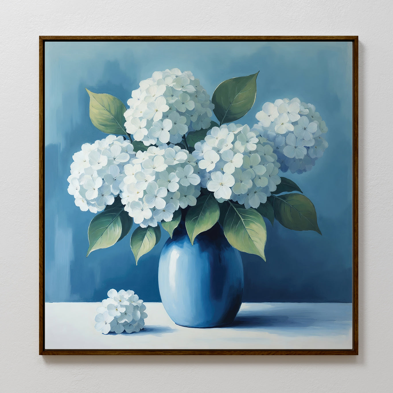 The Azure Cluster Canvas Art depicts white hydrangeas with green leaves in a blue vase against a blue background, with a small hydrangea beside the vase. This framed floral wall art is ideal for enhancing your living room decor.