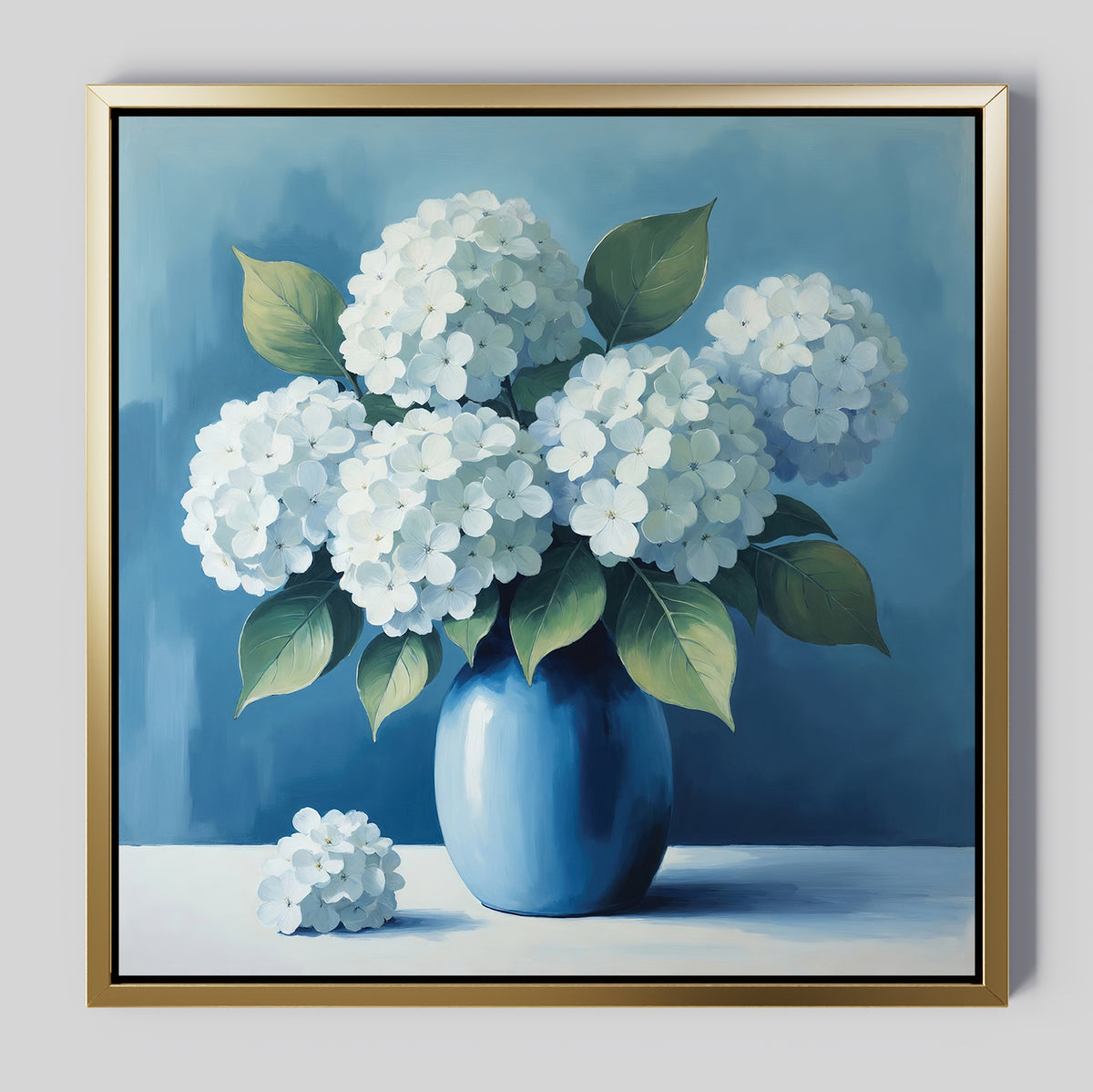 The Azure Cluster Canvas Art features white hydrangea blooms and green leaves in a blue vase set against a blue background—stunning floral wall décor to brighten your living room. A single bloom rests on the white surface next to the vase.