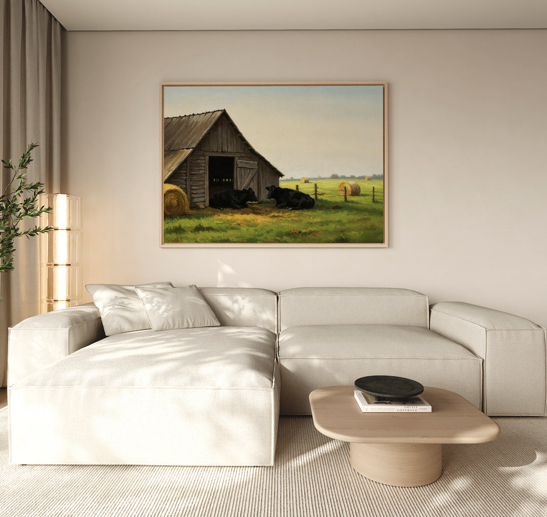 A neutral living room features a cream sectional, light wood coffee table, and “Barnside Rest Canvas Art”—a large farmhouse painting of a barn with cows—hanging above the sofa. Sheer curtains let in natural light.