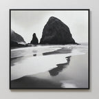 Basalt Beach Canvas Art: a black and white framed photo featuring large rocky sea stacks and reflective wet sand, creating a calm, misty scene—ideal minimalist wall décor for coastal homes.