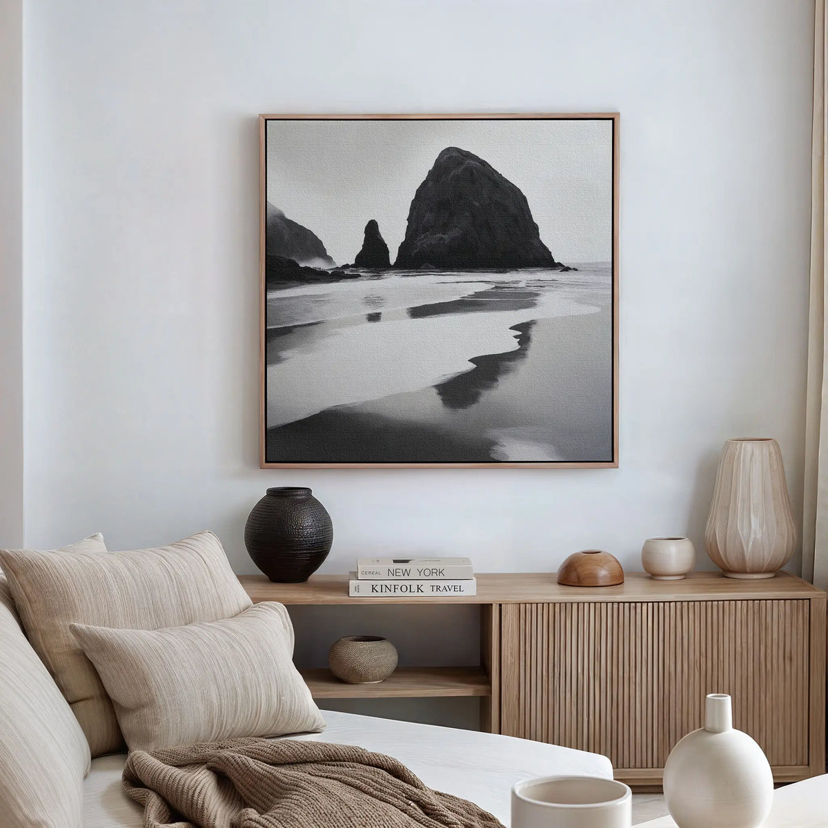A minimalist living room with a beige sofa, neutral pillows, a wooden sideboard, ceramic vases, and the Basalt Beach Canvas Art as black and white wall decor embodies the essence of minimalist coastal style.