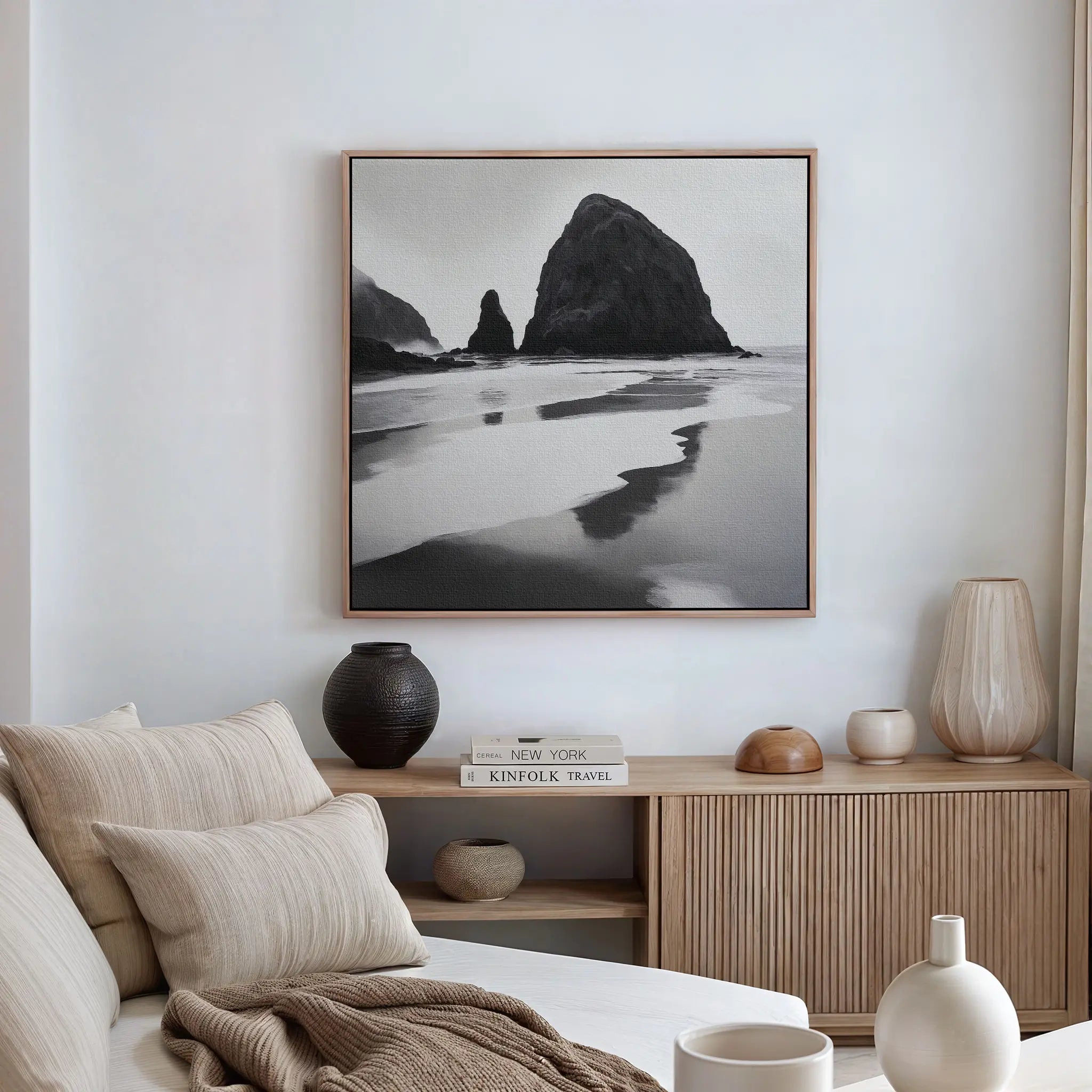 A minimalist living room with a beige sofa, neutral pillows, a wooden sideboard, ceramic vases, and the Basalt Beach Canvas Art as black and white wall decor embodies the essence of minimalist coastal style.