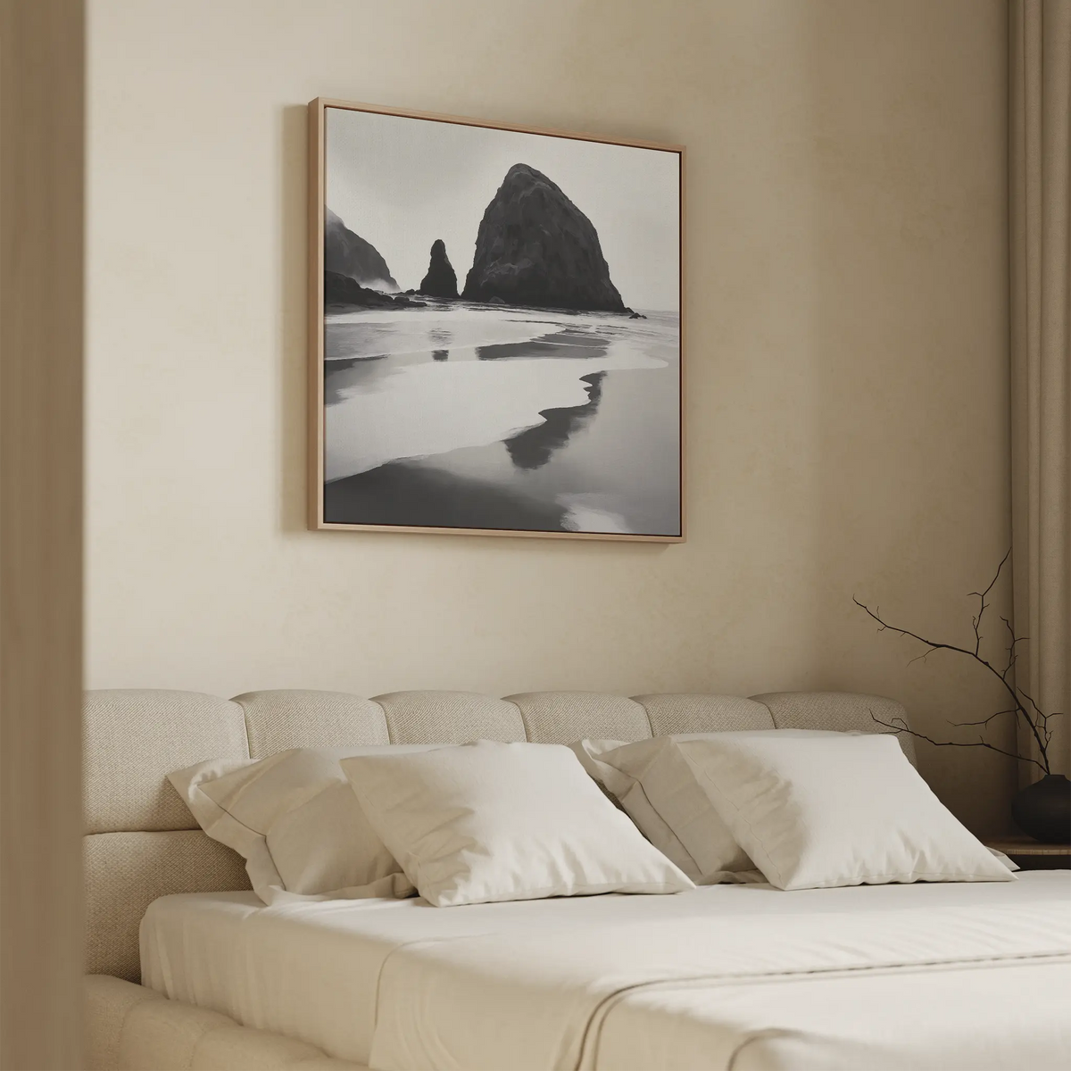 A minimalist bedroom with a beige upholstered bed, white pillows, and the Basalt Beach Canvas Art—a black-and-white beach landscape—framed above the headboard. A bare branch in a vase enhances the serene, understated style.