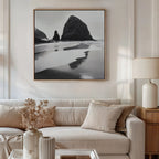 A neutral-toned living room features a beige sofa, cushions, a wooden side table with a white lamp, dried flowers in a vase, and the Basalt Beach Canvas Art above the sofa for a minimalist coastal look.