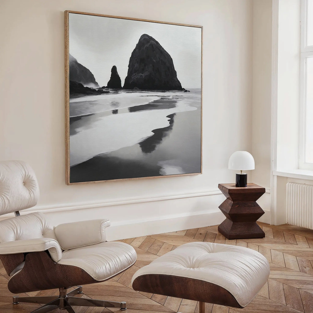 A modern living room with a white lounge chair, wooden side table, and the striking Basalt Beach Canvas Art—a large black and white beach landscape—perfect for minimalist coastal decor lovers.
