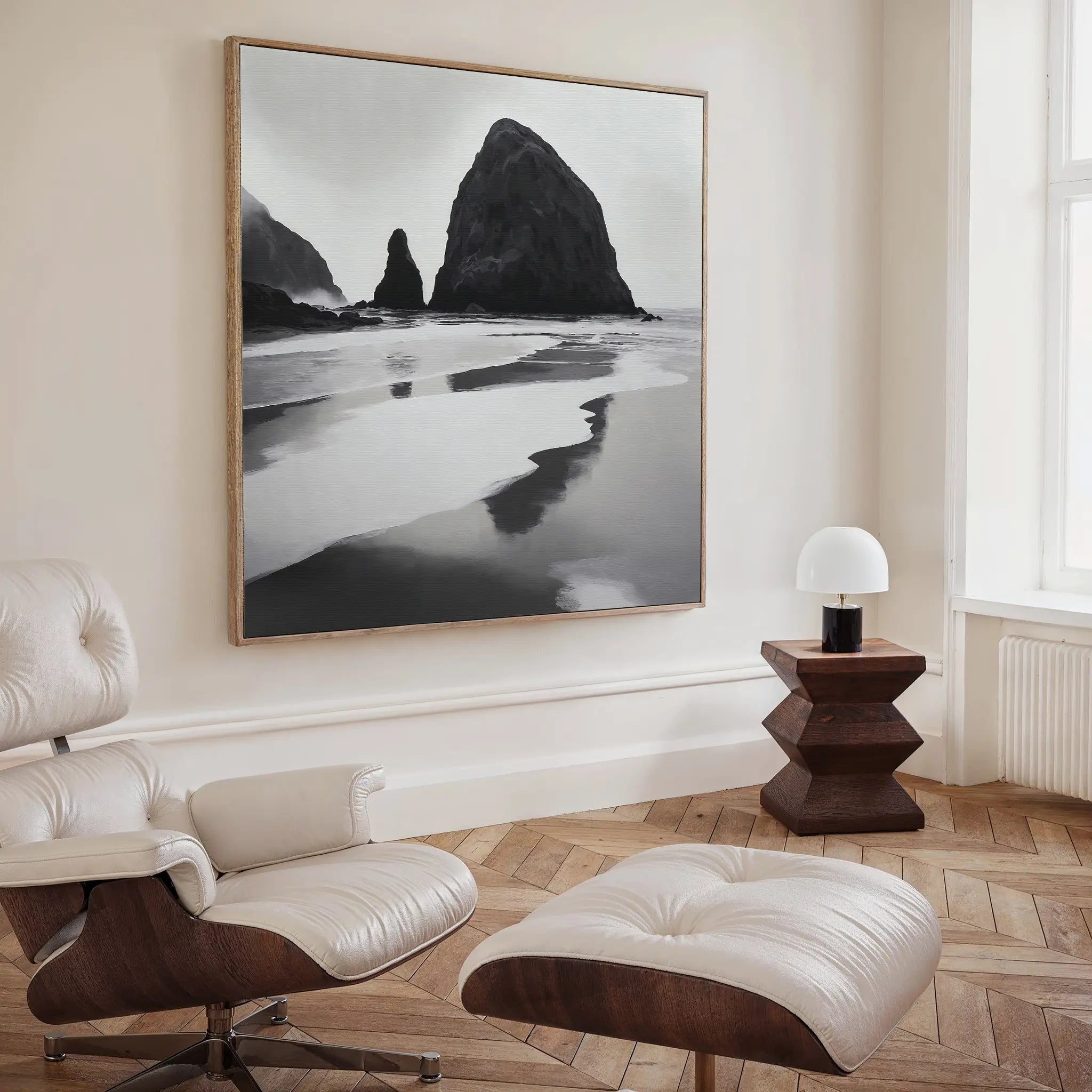 A modern living room with a white lounge chair, wooden side table, and the striking Basalt Beach Canvas Art—a large black and white beach landscape—perfect for minimalist coastal decor lovers.