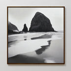 Basalt Beach Canvas Art: A framed black and white coastal scene featuring large sea stacks reflected in wet sand under an overcast sky, perfect as modern wall art for any bedroom.