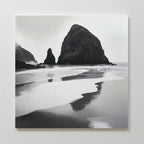 Basalt Beach Canvas Art features black and white wall art of a rocky coast with sea stacks reflected in wet sand under cloudy skies. This minimalist piece adds a calm, moody touch to modern bedrooms and looks stunning on a white wall.