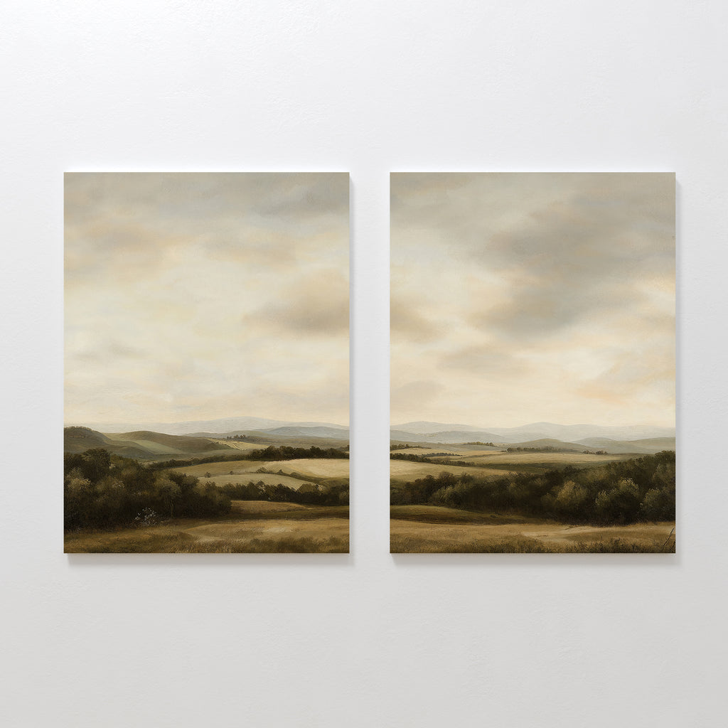 The Beneath The Clouds Set of 2 features minimalist wall art canvases, each depicting serene landscapes with rolling hills, fields, and distant mountains under a cloudy sky in soft, earthy tones.