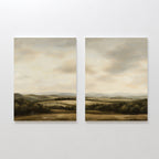 The Beneath The Clouds Set of 2 features minimalist wall art canvases, each depicting serene landscapes with rolling hills, fields, and distant mountains under a cloudy sky in soft, earthy tones.