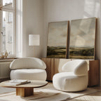 A modern living room features two rounded white armchairs, a low wooden coffee table, a floor lamp, and the Beneath The Clouds Set of 2 wall art prints on a wooden cabinet by the window. Natural light brightens the cozy space.
