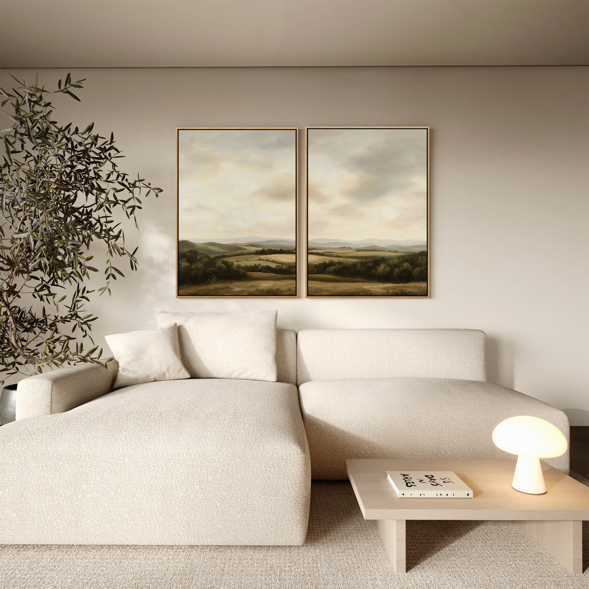 A modern living room with a textured cream sectional sofa, wooden coffee table holding a lamp and book, potted plant, and the Beneath The Clouds Set of 2 minimalist wall art canvases hanging on the beige wall.