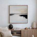 A minimalist living room featuring a beige sofa, neutral cushions, wooden sideboard, decorative vases, and Binary Calm Abstract Canvas Art—a black and beige piece—bringing modern elegance to the serene white wall.