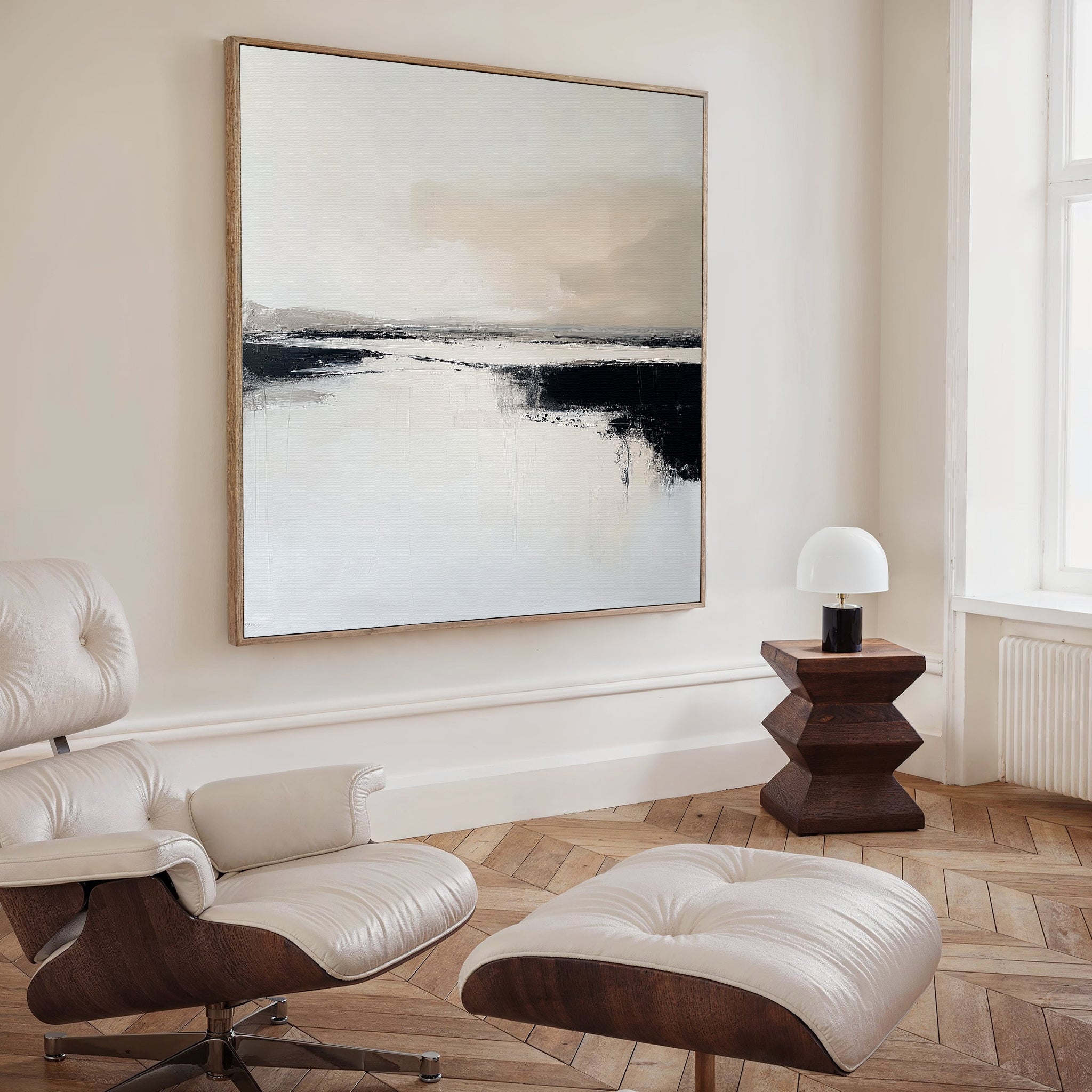 A modern, minimalist living room features a cream leather lounge chair with ottoman, light wood herringbone floors, white walls, a wooden side table with a white lamp, and the Binary Calm Abstract Canvas Art in neutral tones for elegant style.