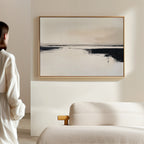 A woman in a white outfit stands in a modern, minimal space, admiring the Binary Calm Abstract Canvas Art – Horizontal with soft, neutral tones displayed above a light-colored sofa.
