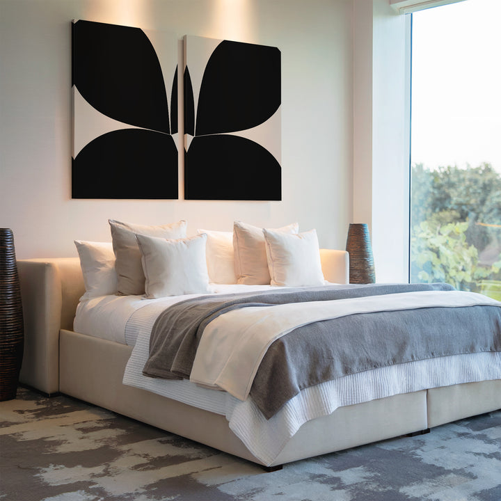 A modern bedroom with a large bed in white and gray bedding, four white pillows, tall decorative vases, a big window with greenery views, and the Minimal Petal Set of 2—abstract black minimalist wall art above the bed.