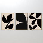 The Black Botanical Set of 3 features minimalist art prints with abstract black leaf designs on beige backgrounds, each framed in light wood and displayed side by side for striking botanical wall art.