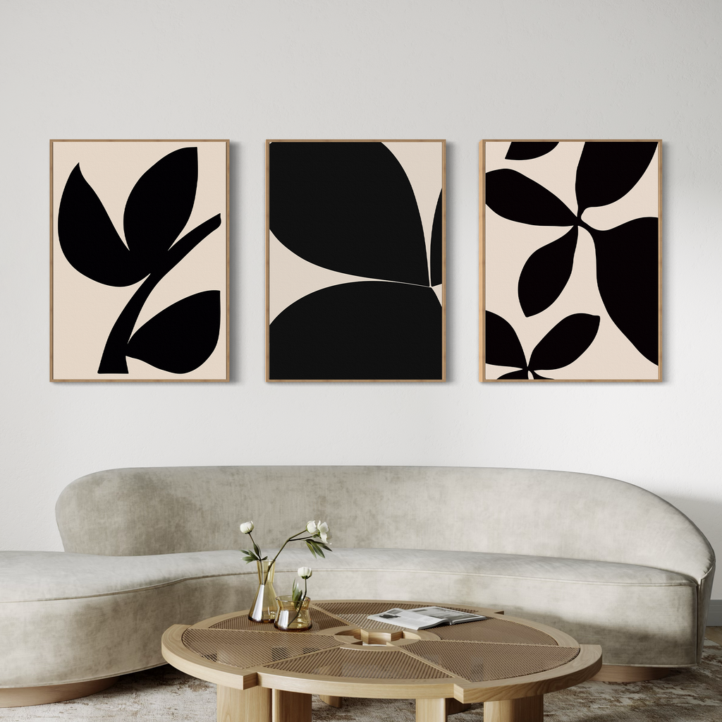 A modern living room with a curved beige sofa, a round wooden coffee table, and the Black Botanical Set of 3—abstract black-and-beige botanical wall art prints from Nordic Park—displayed above the sofa.