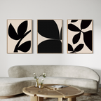 A modern living room with a curved beige sofa, a round wooden coffee table, and the Black Botanical Set of 3—abstract black-and-beige botanical wall art prints from Nordic Park—displayed above the sofa.