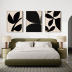 A modern bedroom features an olive green bed with white bedding, two beige nightstands with lamps, and the Black Botanical Set of 3—minimalist black and white abstract leaf prints inspired by Nordic Park—displayed above the bed.