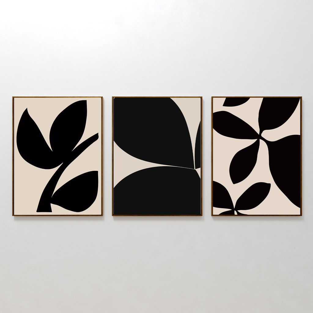 The Black Botanical Set of 3 features framed wall art prints with bold black leaf shapes on beige backgrounds, each showcasing a unique minimalist leaf design and displayed side by side on a white wall.
