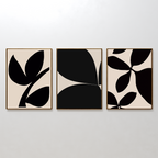The Black Botanical Set of 3 features framed wall art prints with bold black leaf shapes on beige backgrounds, each showcasing a unique minimalist leaf design and displayed side by side on a white wall.