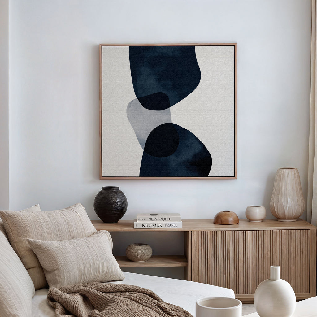 A minimalist living room with a beige sofa, striped cushions, a wooden cabinet decorated with vases and books, and striking modern wall art—Blue Currents Canvas Art—featuring dynamic organic shapes in black and gray.