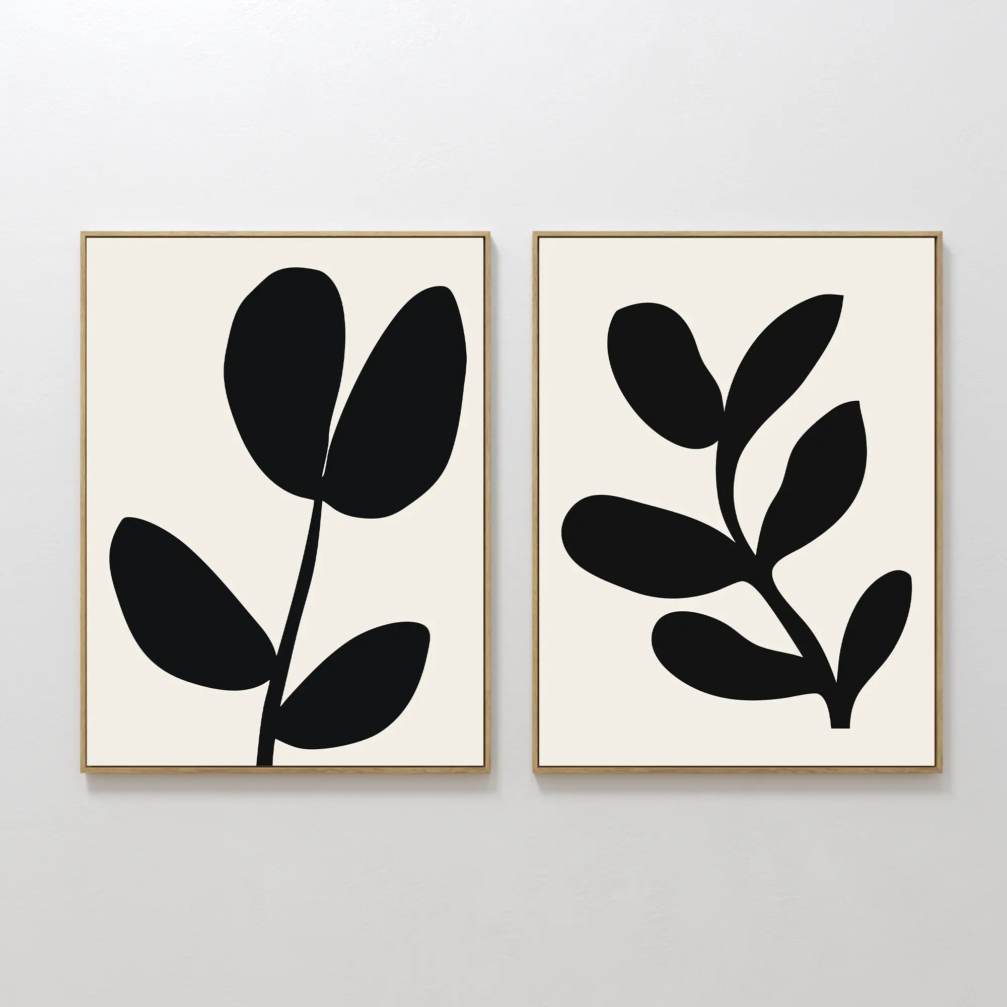 The Black Leaf Set of 2 features framed minimalist prints with abstract black leaf shapes on a white background, each showcasing a simple botanical design—perfect for striking botanical wall art.