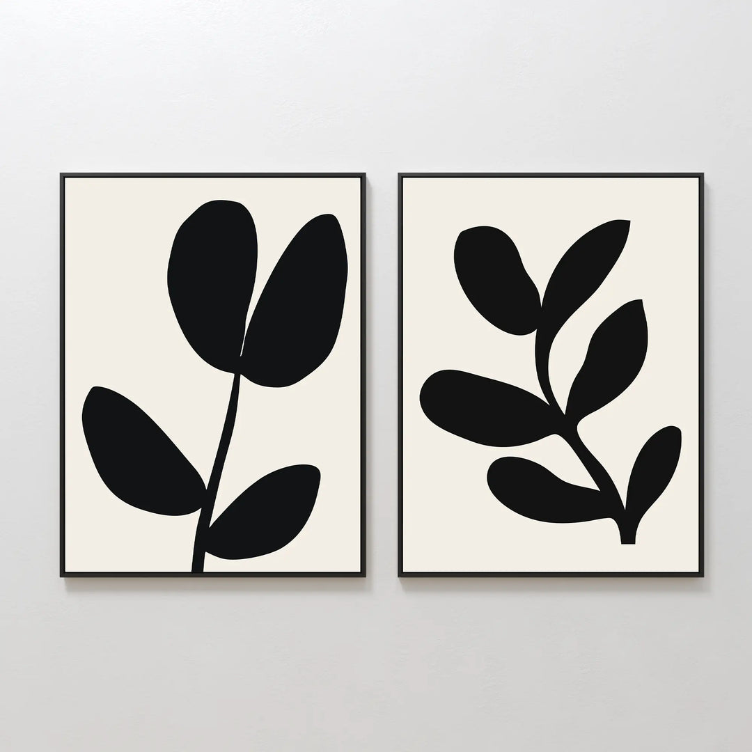 The Black Leaf Set of 2 features framed minimalist prints, each with striking black botanical silhouettes—three leaves on one, five on the other—set against light backgrounds. Perfect for fans of minimalist or botanical wall art.
