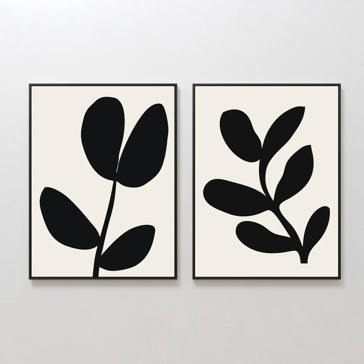 The Black Leaf Set of 2 features framed minimalist prints, each with striking black botanical silhouettes—three leaves on one, five on the other—set against light backgrounds. Perfect for fans of minimalist or botanical wall art.