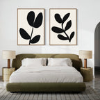 A modern bedroom with a low olive green bed, two round beige nightstands topped with matching lamps, and the Black Leaf Set of 2 minimalist prints hanging above the bed on a crisp white wall.