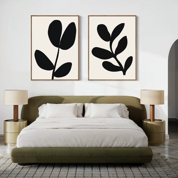A modern bedroom with a low olive green bed, two round beige nightstands topped with matching lamps, and the Black Leaf Set of 2 minimalist prints hanging above the bed on a crisp white wall.