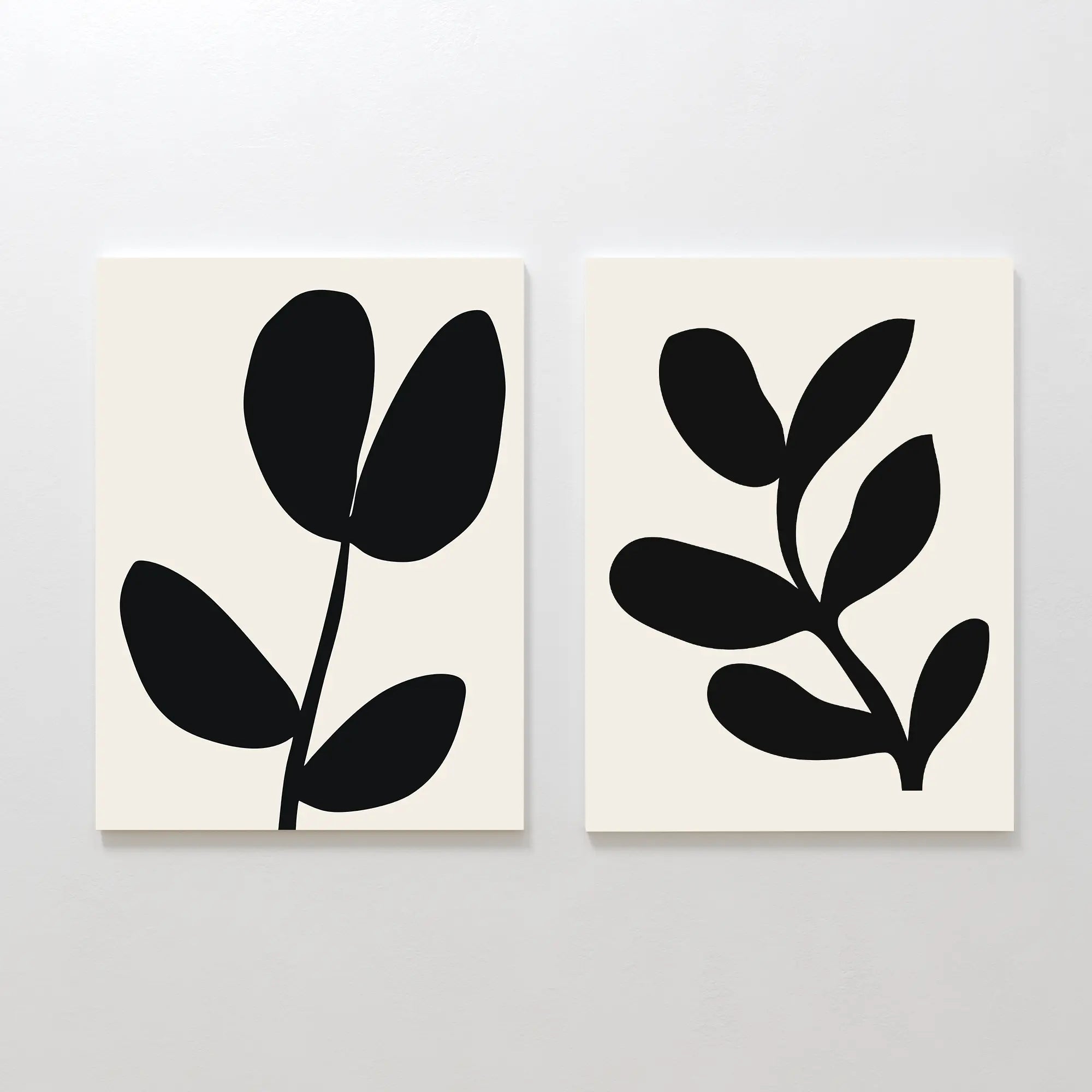 The Black Leaf Set of 2 features minimalist prints with bold black abstract plant silhouettes, each showing a stylized stem with rounded leaves—perfect botanical wall art for modern decor.