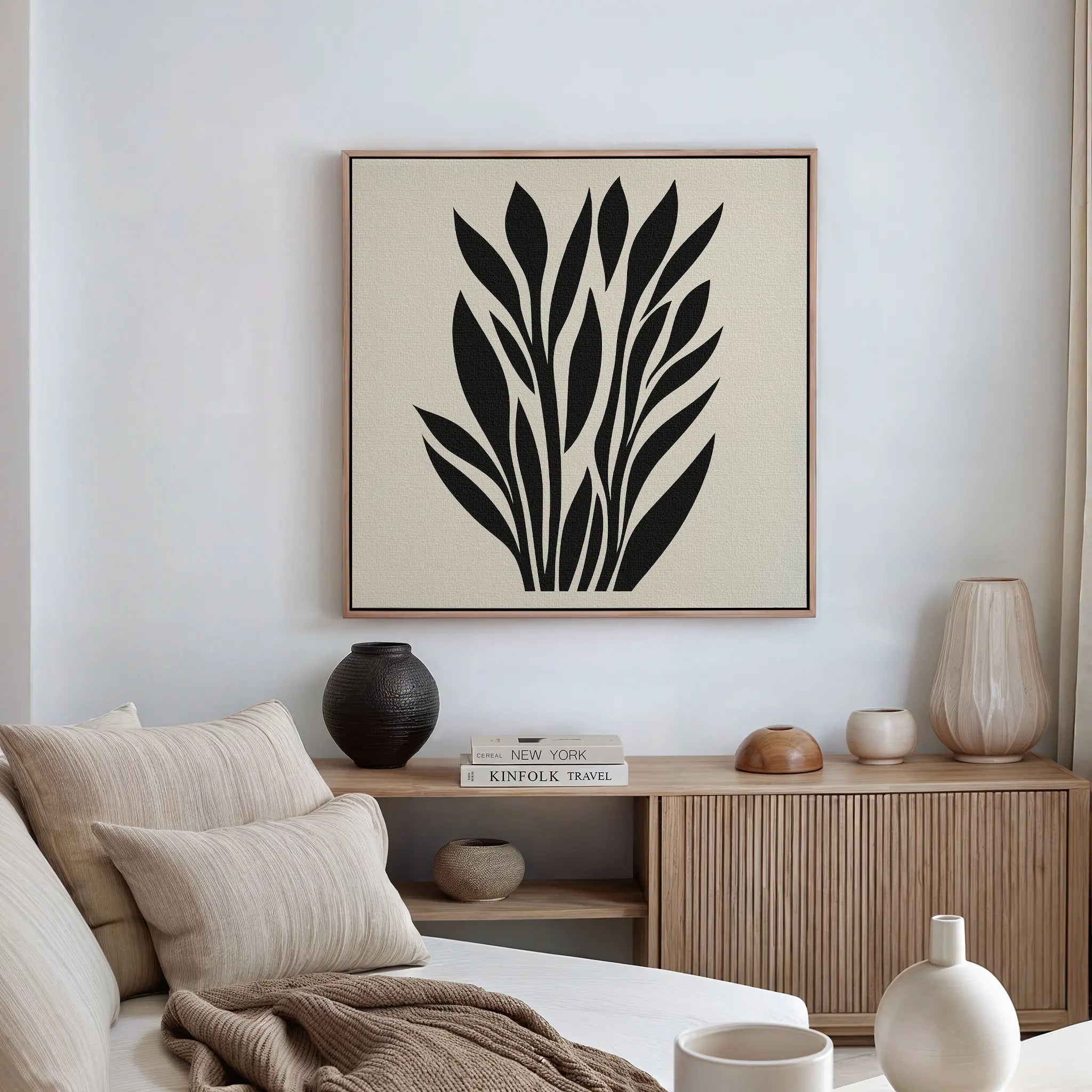A modern, minimalist living room features a white wall, neutral sofa, wooden sideboard, decorative vases, and the Black Palm Study Canvas Art with abstract black palm leaves hanging above the sideboard.