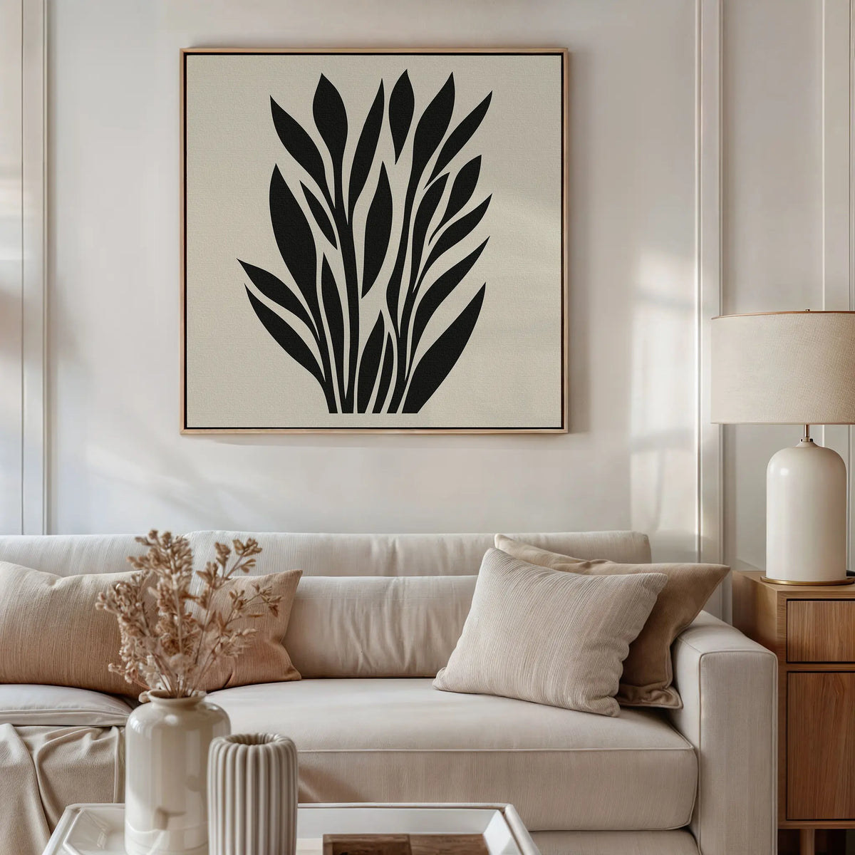 A modern living room with a beige sofa, neutral cushions, a wooden side table and white lamp, minimalist decor, and the Black Palm Study Canvas Art with abstract black palm leaves displayed above the sofa.