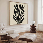 A modern living room features a cream lounge chair and ottoman, a side table with a white lamp, and the Black Palm Study Canvas Art. Light wood herringbone floors and large windows complete this stylish interior.