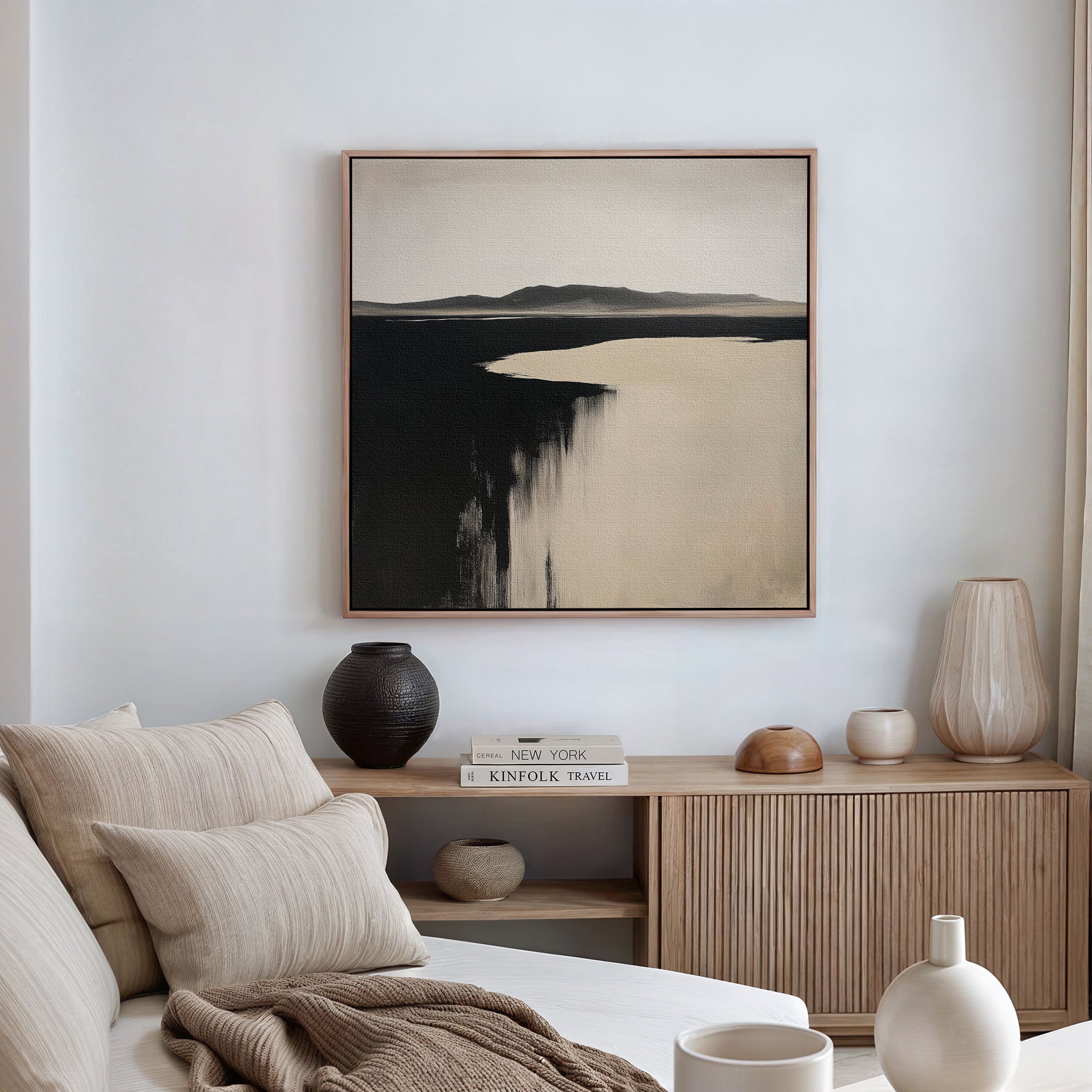 A minimalist living room features a beige sofa, striped cushions, and neutral décor. Above the wooden console hangs Black Shore Canvas Art—a large abstract painting in black and beige, ideal for modern living room decor.